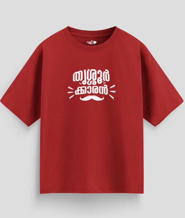 Red oversized unisex T-shirt with Malayalam text "Thrissurkaran" and mustache graphic in white print, representing Thrissur culture.